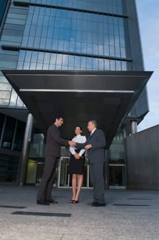 Two businessmen shaking hands in front of an office building
