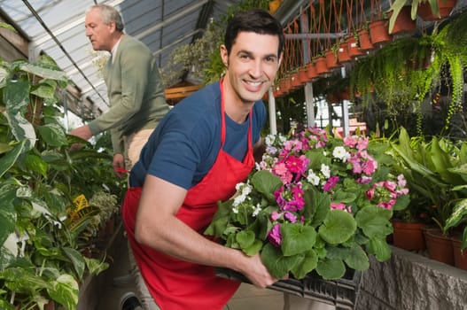 Man holding a crate of plants in a garden center with a customer in the background
