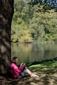 Side profile of a young woman leaning against a tree and text messaging