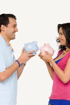 Side profile of a young couple holding piggy banks and smiling