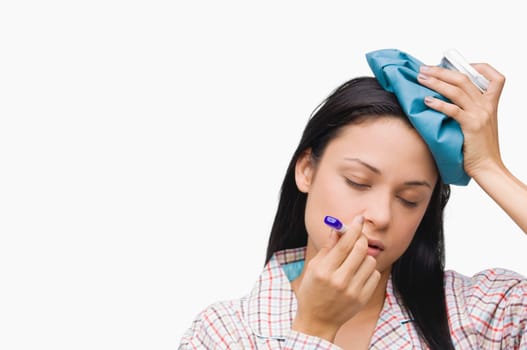 Close-up of a young woman measuring her temperature with a thermometer and holding an ice pack on her head