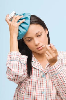 Close-up of a young woman measuring her temperature with a thermometer and holding an ice pack on her head