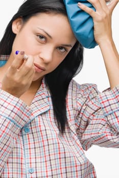 Portrait of a young woman measuring her temperature with a thermometer and holding an ice pack on her head