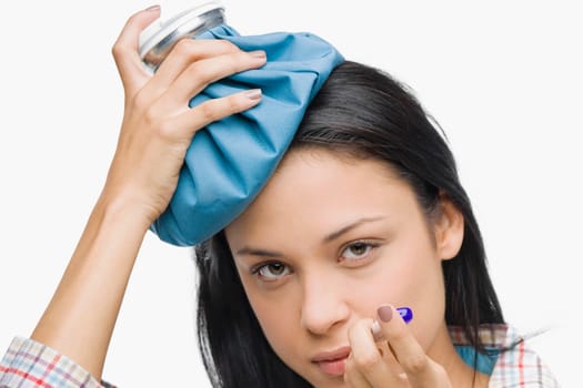 Portrait of a young woman measuring her temperature with a thermometer and holding an ice pack on her head