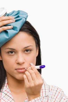 Portrait of a young woman measuring her temperature with a thermometer and holding an ice pack on her head