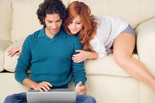 Young man using a laptop with a young woman leaning over him