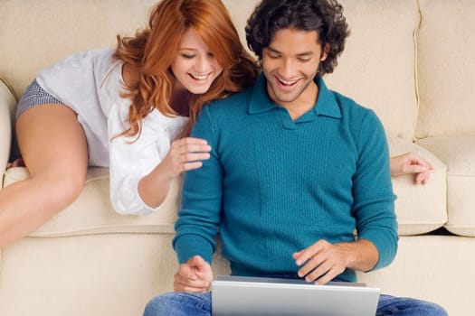 Young man using a laptop with a young woman leaning over him