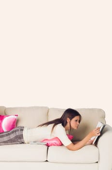 Side profile of a young woman lying on a couch and reading a book