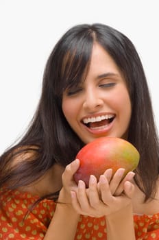 Close-up of a young woman holding a mango and laughing