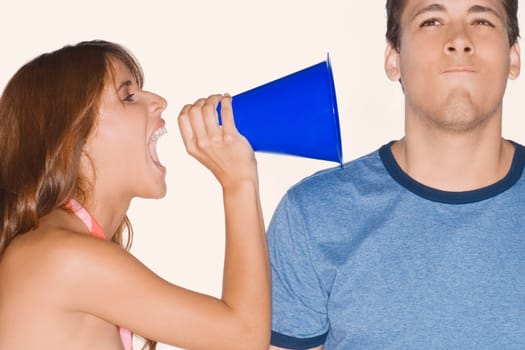 Side profile of a young woman shouting with a megaphone into a young man's ear