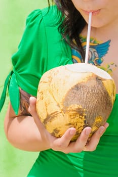 Mid section view of a young woman drinking coconut milk with a drinking straw