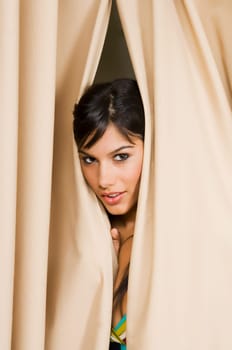 Portrait of a young woman peeking through a curtain