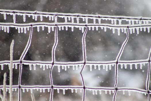 Close up of ice covers wire fence with ice icicles . High quality photo