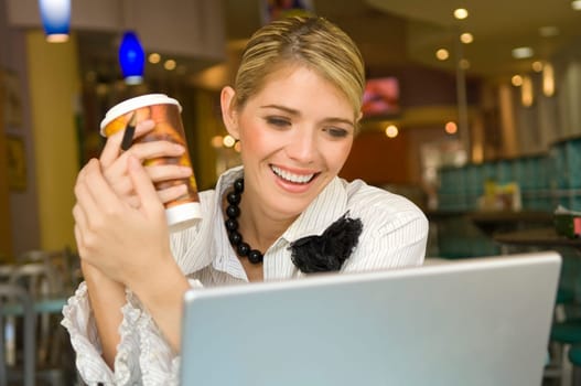 Businesswoman looking at a laptop and holding a disposable cup in a restaurant