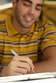 Close-up of a young man writing on a diary and smiling