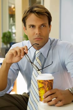 Businessman sitting in a restaurant and holding a disposable cup