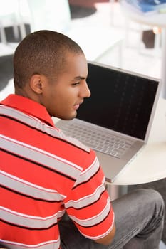 Rear view of a young man sitting at a cafe with a laptop in front of him