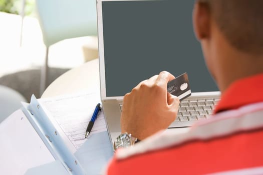 Rear view of a young man using a laptop and holding a credit card