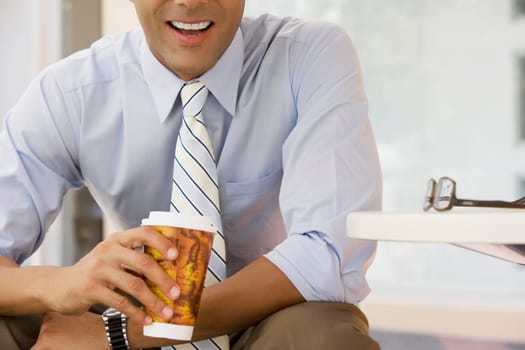Mid section view of a businessman holding a coffee cup and smiling