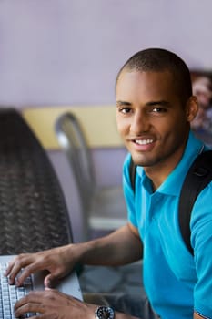 Portrait of a young man using a laptop in a cafe and smiling
