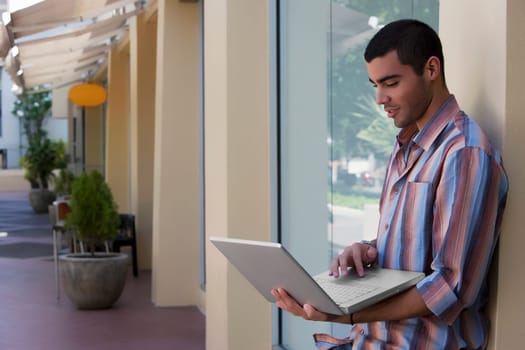 Side profile of a young man leaning against the wall and using a laptop