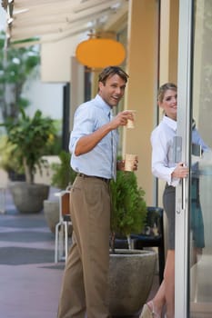 Portrait of a businessman holding two cups of coffee and standing near a businesswoman