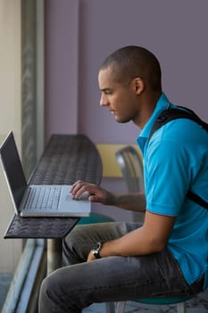 Side profile of a young man using a laptop in a cafe
