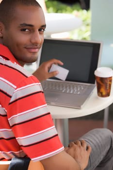Portrait of a young man sitting at a cafe and holding a credit card