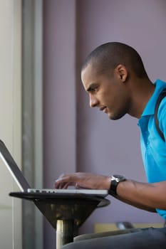 Side profile of a young man using a laptop in a cafe