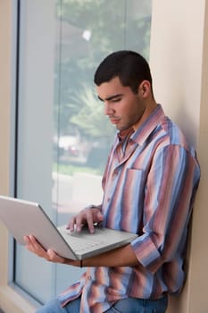 Side profile of a young man leaning against the wall and using a laptop