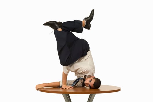 Portrait of a businessman doing a handstand on a table with a mobile phone in his mouth