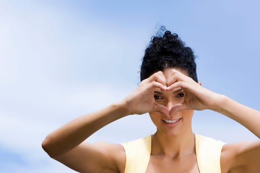 Portrait of a young woman making a heart shape in front of her face and smiling