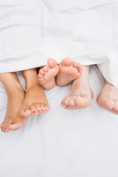 High angle view of a couple's feet with their child on the bed