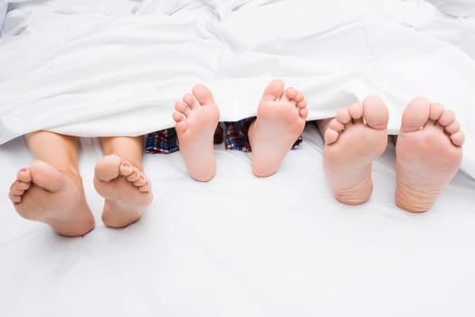 Close-up of a couple's feet with their child on the bed
