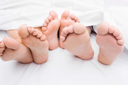 Close-up of a couple's feet with their child on the bed