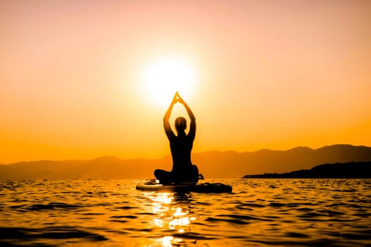 A girl at sunset on a paddleboard is engaged in yoga. hands up at sunset.