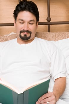 Mid adult man reclining on the bed and reading a book
