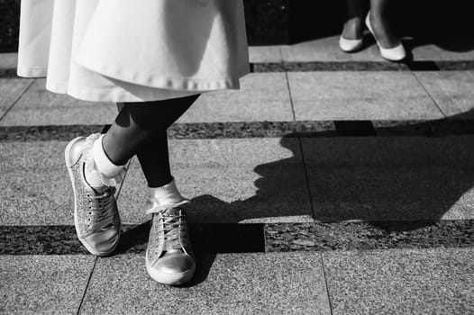 Black white photo, a girl in a white dress and sneakers on the tile of the sidewalk.