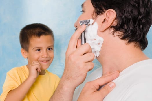 Boy looking at his father shaving in the bathroom