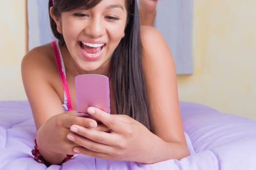 Close-up of a teenage girl lying on the bed and text messaging on a mobile phone