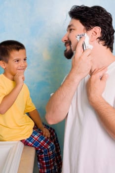 Boy looking at his father shaving in the bathroom