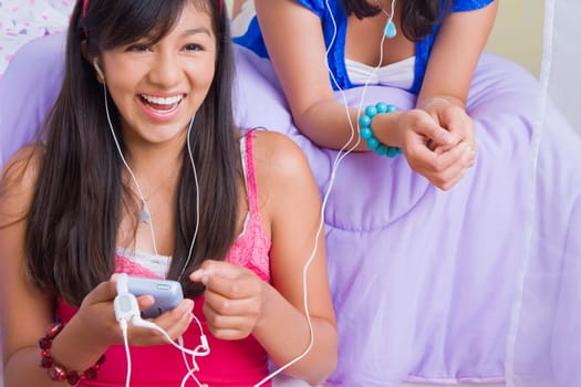 Close-up of a teenage girl and a young woman listening to music with ear buds and smiling