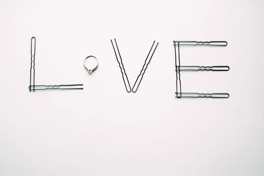 The word love is made of hairpins and an engagement ring.