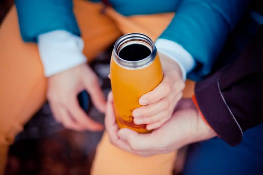 Orange thermos in the hands of a man.