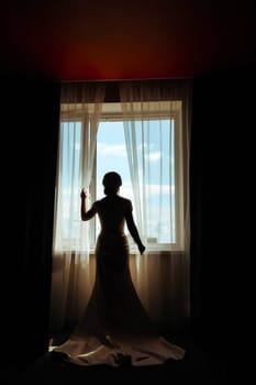 The bride in a dress by the window and looks out the window.