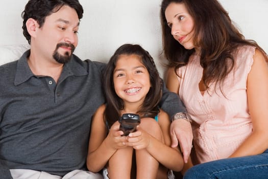 Portrait of a girl holding a remote control with her parents sitting beside her