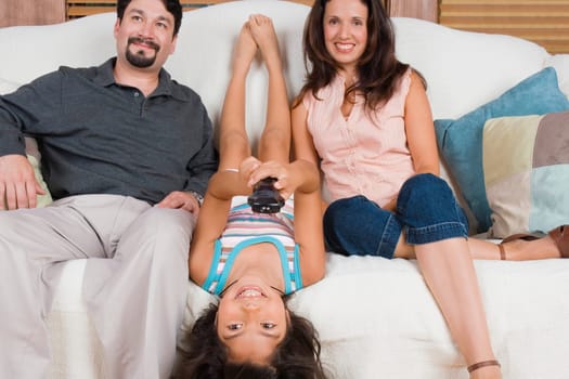 Mid adult couple sitting on a couch with their daughter lying on a couch between them and smiling
