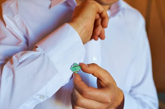 A man wears a cufflink on a white shirt.