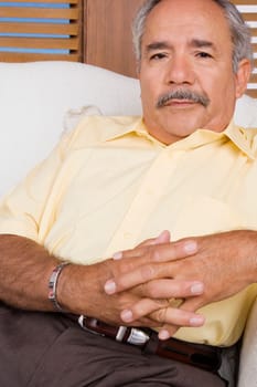 Portrait of a senior man sitting on a couch with his hands clasped