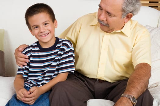 Portrait of a boy sitting with his grandfather on a couch and smiling